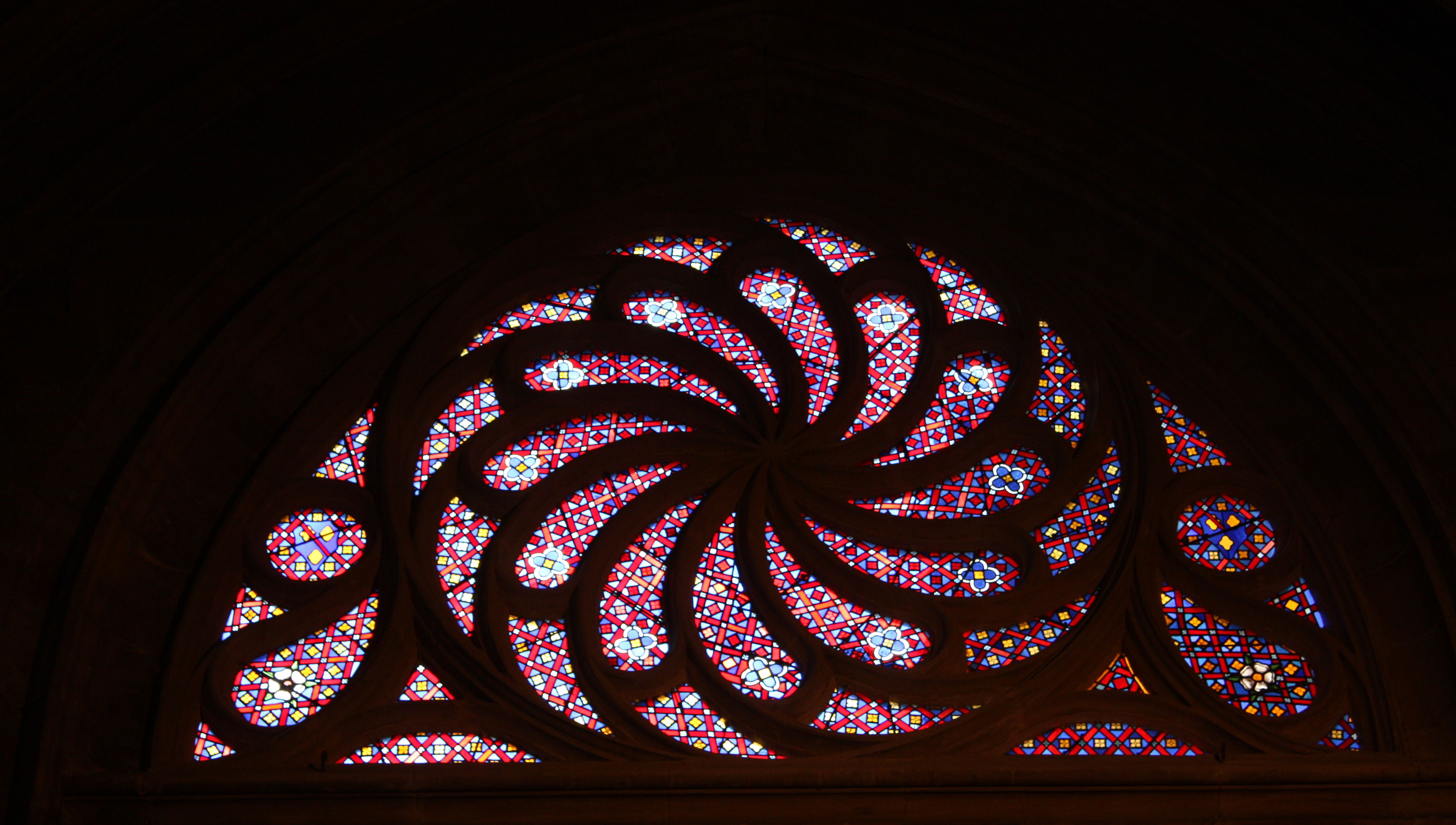 Ein farbenfrohes Kirchenfenster, das ein verschnörkeltes Blumenmuster zeigt. Die Umrisse sind dunkel.