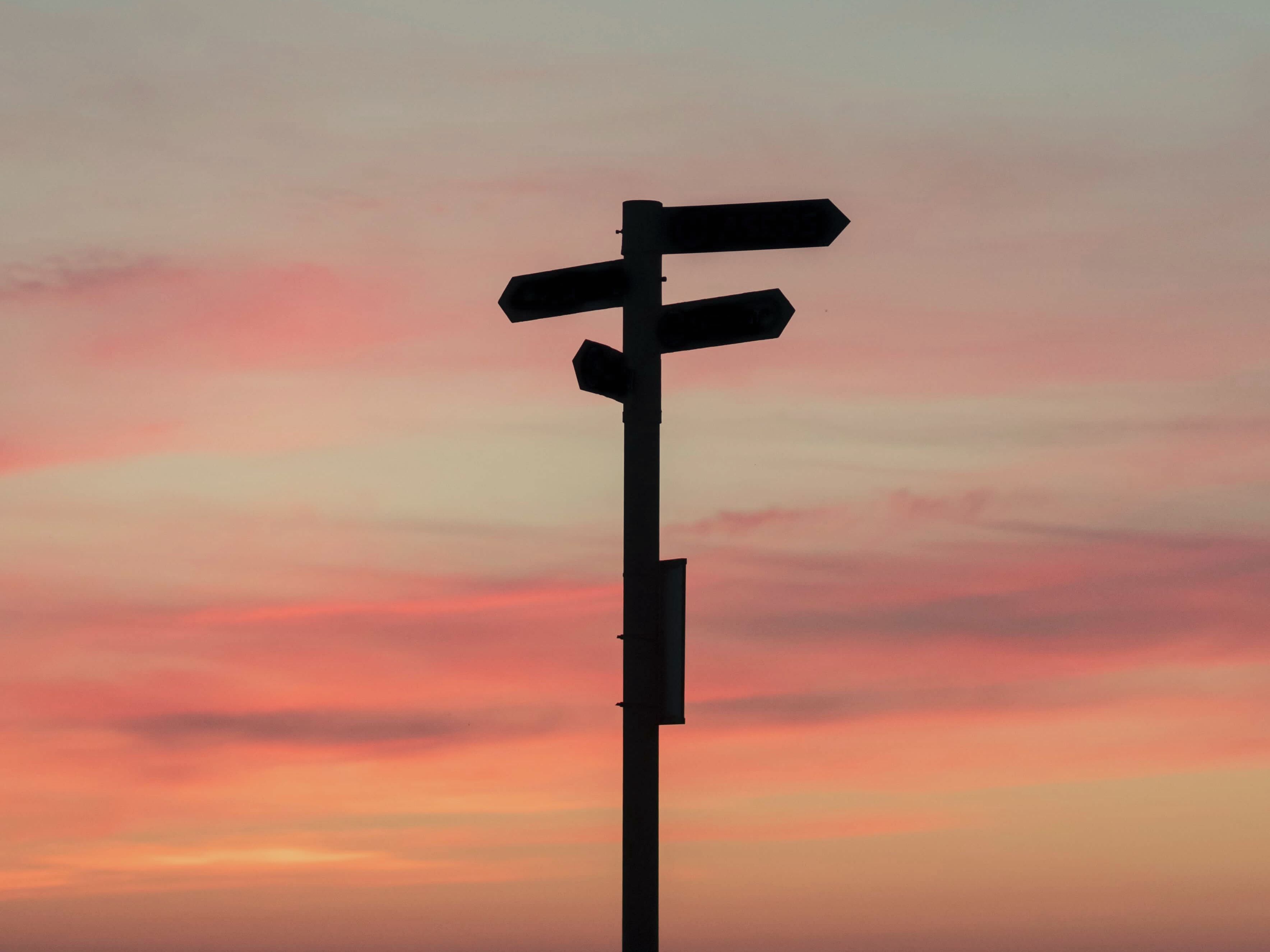 Ein Wegweiser steht im Abendrot und zeigt in verschiedene Richtungen