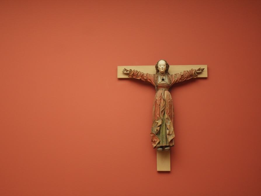 Ein kleines, dekoratives Holzkreuz an einer rot-orangenen Wand